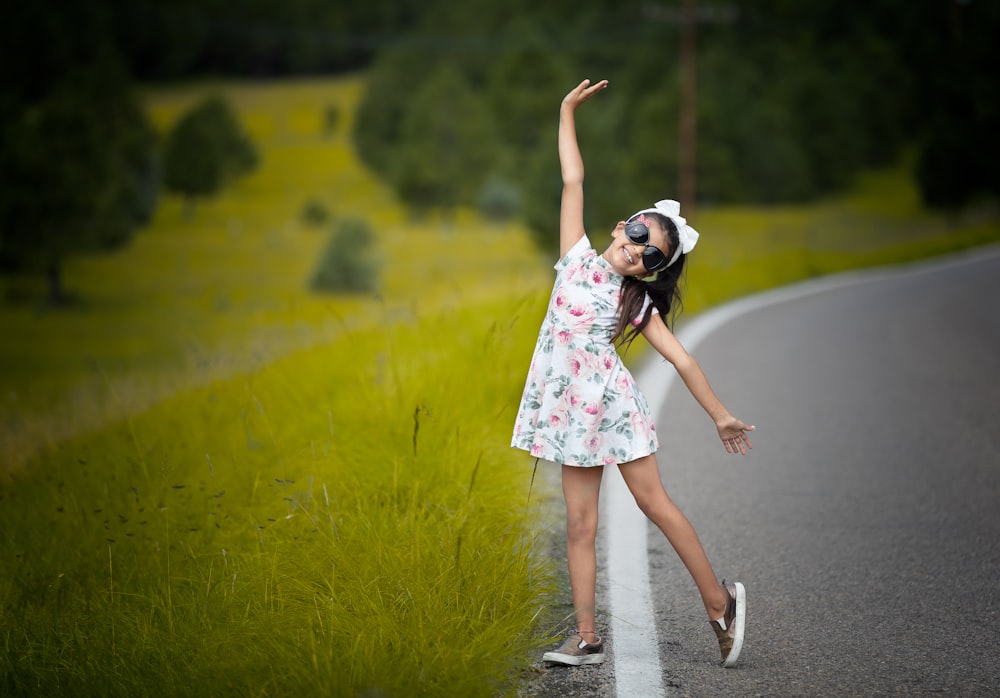 a girl in a white dress is dancing on the side of the road