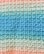 A close-up view of a crocheted fabric with a pattern of alternating colors. The texture shows a consistent and repetitive stitching pattern, transitioning smoothly from light blue to various shades of green and finally to peach.