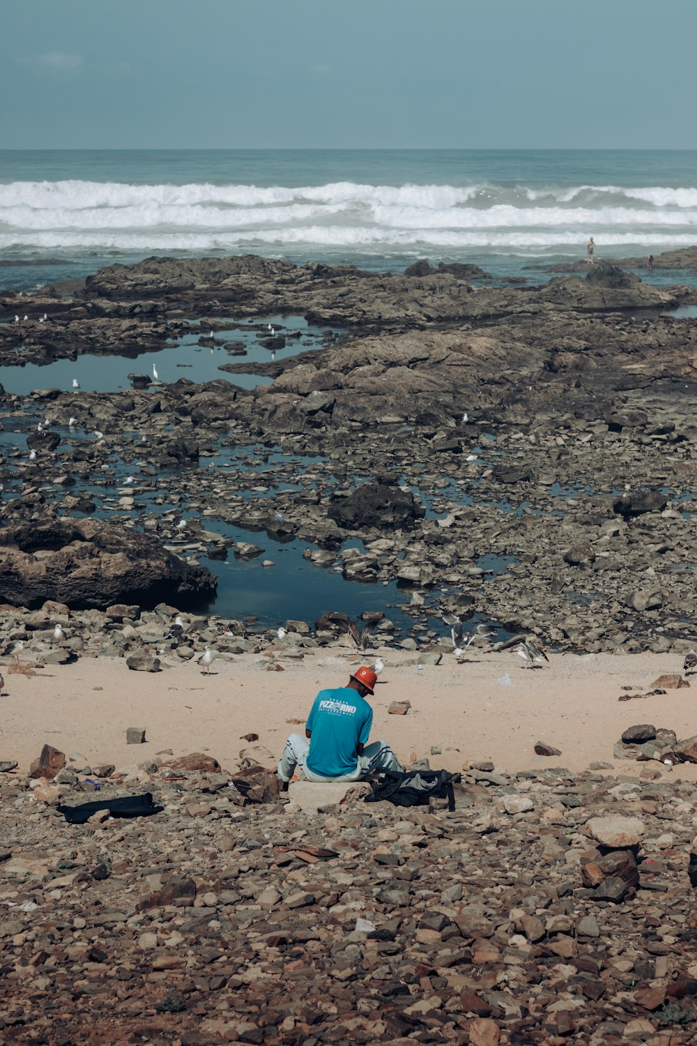 海の隣の岩だらけのビーチに座っている男