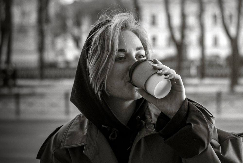 a woman drinking from a coffee cup in a park