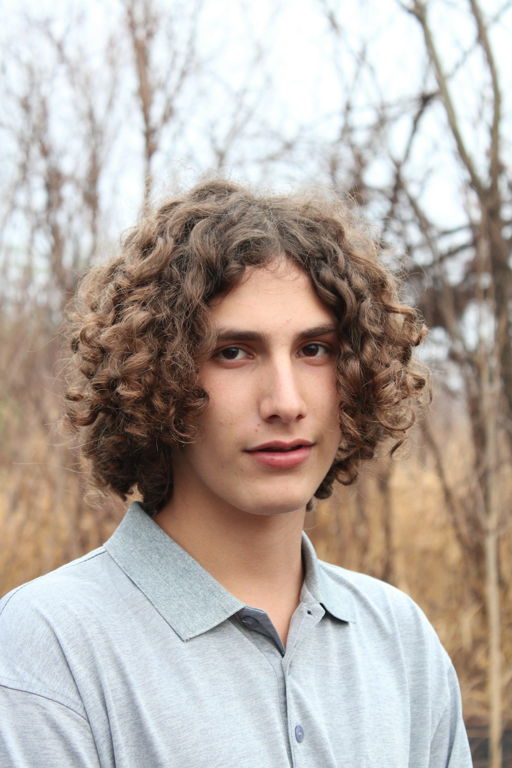 a young man with curly hair standing in front of trees