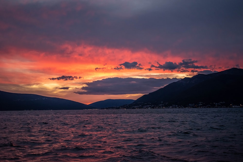 un coucher de soleil sur un plan d’eau avec des montagnes en arrière-plan