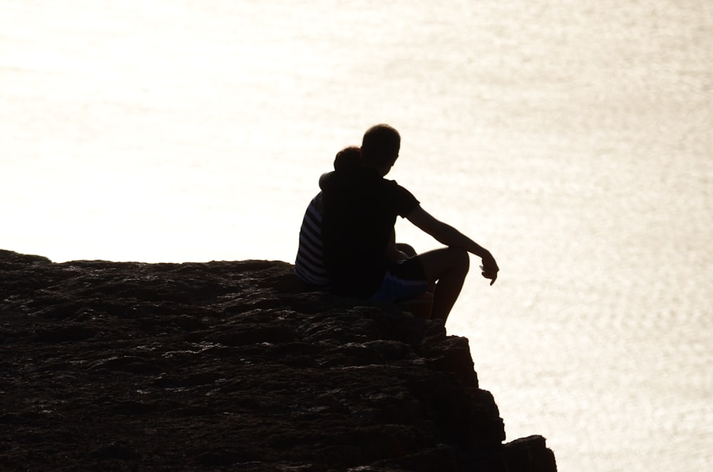 eine Person, die auf einer Klippe mit Blick auf ein Gewässer sitzt