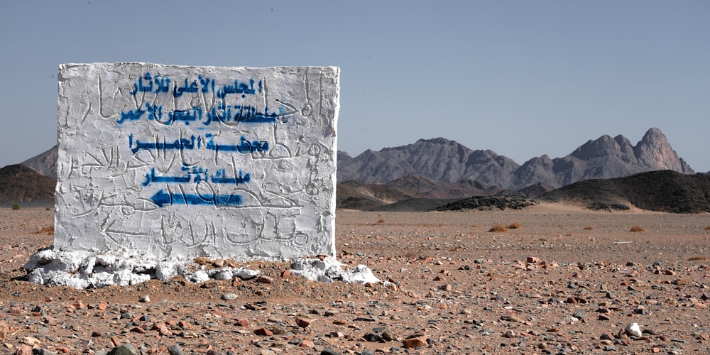 a sign in the middle of a desert with mountains in the background