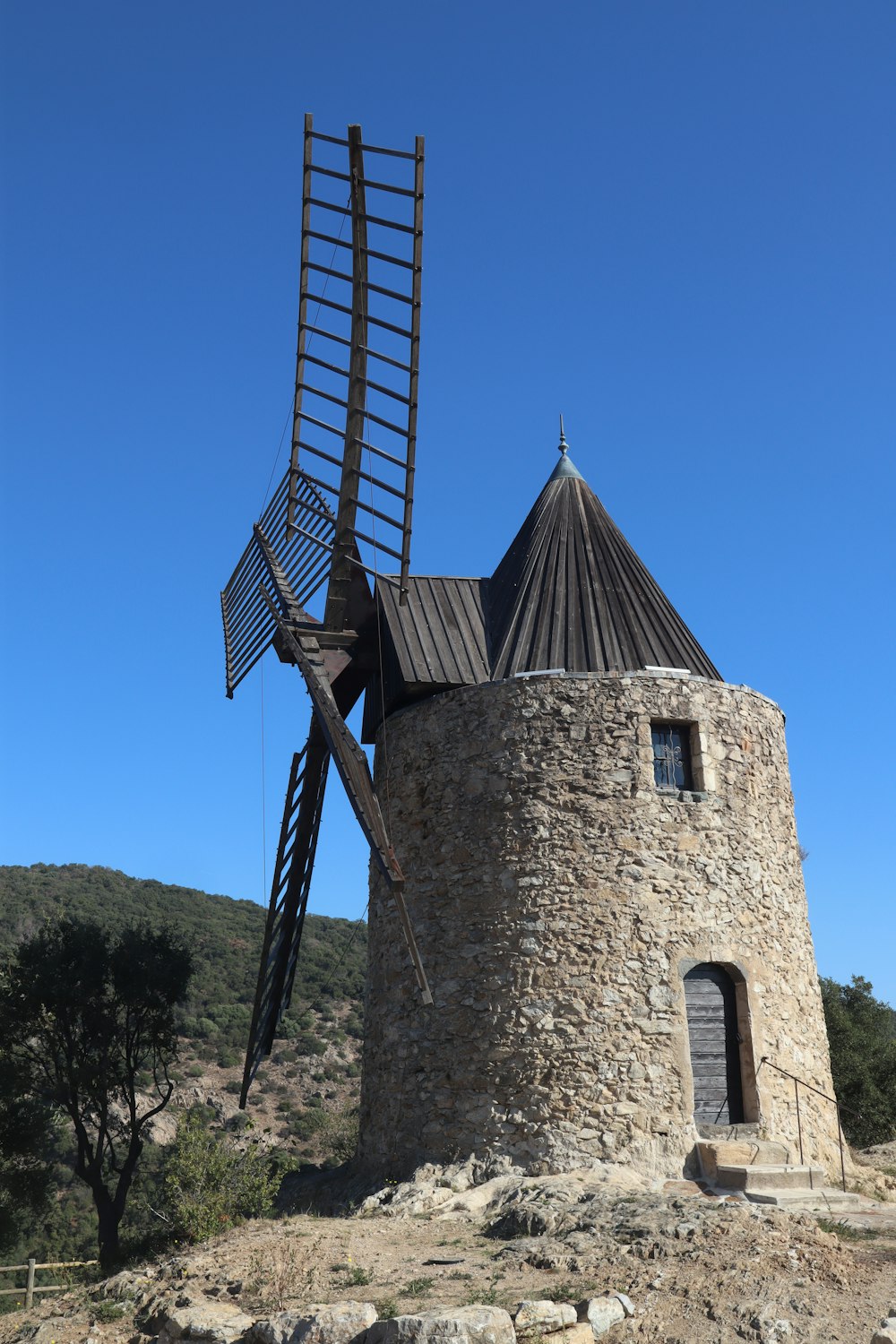 um moinho de vento de pedra com um telhado de madeira no topo de uma colina