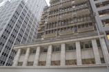 Several high-rise office buildings with a modern architectural style are arranged closely together. The facade of the buildings consists of glass and metal, featuring rows of windows. The structure is complemented by some signs with gold-colored Chinese characters on one building.