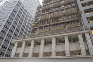 Several high-rise office buildings with a modern architectural style are arranged closely together. The facade of the buildings consists of glass and metal, featuring rows of windows. The structure is complemented by some signs with gold-colored Chinese characters on one building.