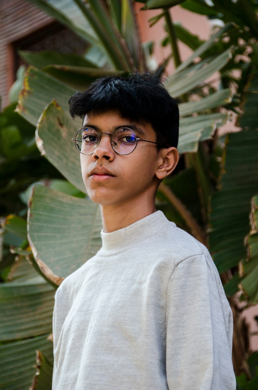 a young boy wearing glasses standing in front of a plant