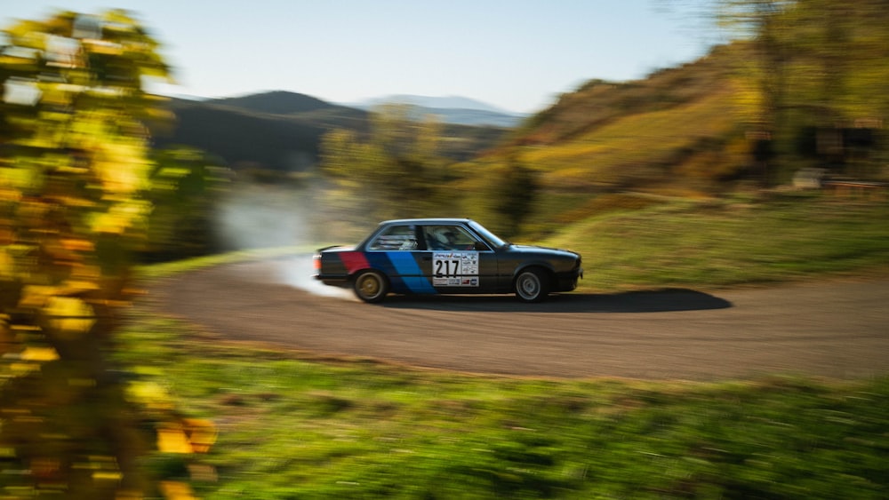 a blue car driving down a road next to a lush green hillside