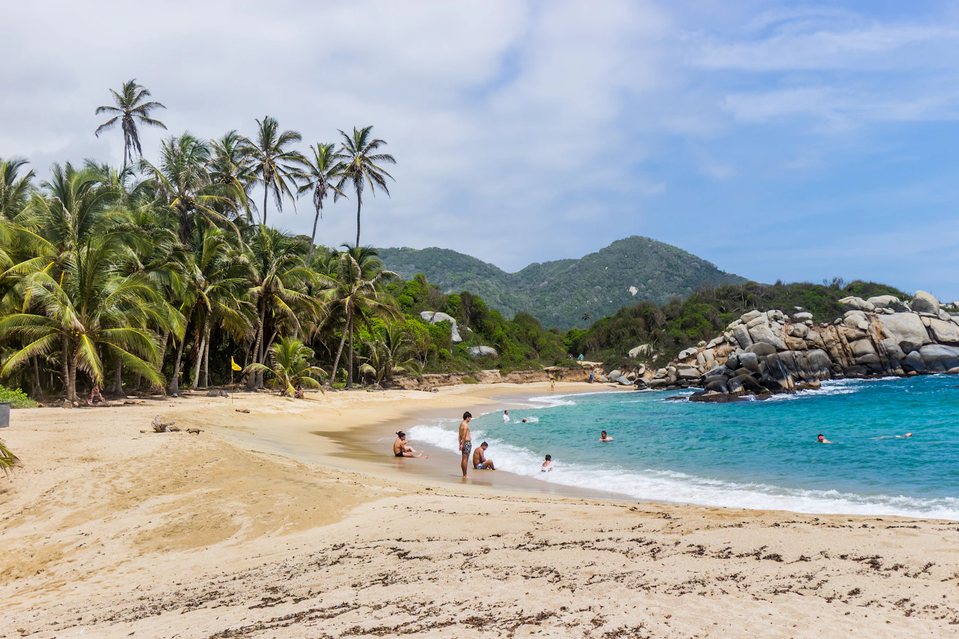 A golden palm-fringed Tayrona beach with turquoise Caribbean water and a jungle hill behind