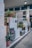 Multiple fuel pumps lined up at a gas station adorned with potted plants. The pumps have colorful nozzles and are positioned under a covered area with overhead lighting. Walls feature signs offering free car washes.