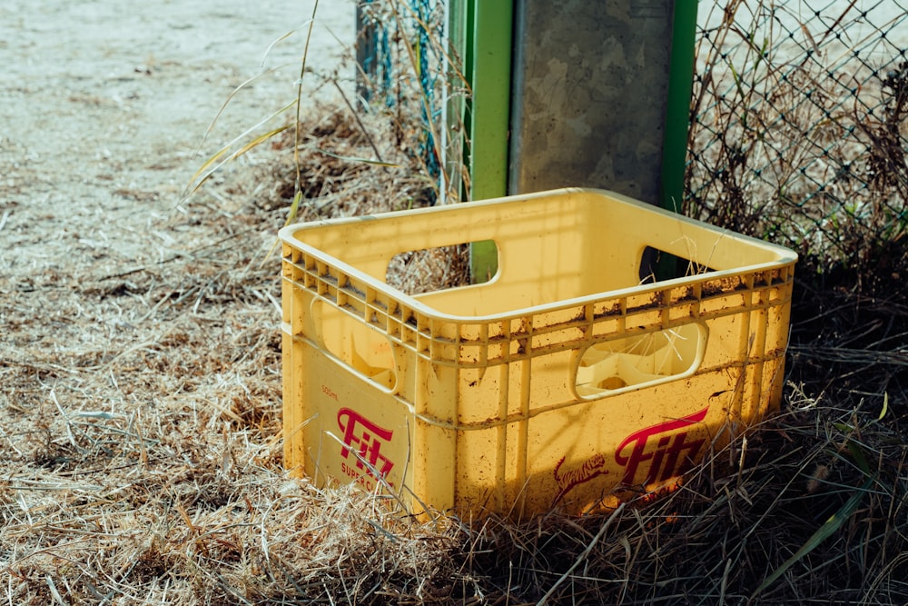 a yellow crate sitting in the grass next to a fence