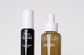 Two skincare bottles are positioned side by side against a plain background. The black bottle on the left is labeled 'Mito Special' and described as a cell booster. The brown bottle on the right, labeled 'Cells Life', features a dropper cap and is described as a repairing concentrate.