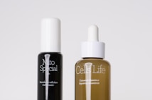 Two skincare bottles are positioned side by side against a plain background. The black bottle on the left is labeled 'Mito Special' and described as a cell booster. The brown bottle on the right, labeled 'Cells Life', features a dropper cap and is described as a repairing concentrate.