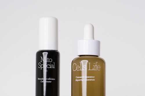 Two skincare bottles are positioned side by side against a plain background. The black bottle on the left is labeled 'Mito Special' and described as a cell booster. The brown bottle on the right, labeled 'Cells Life', features a dropper cap and is described as a repairing concentrate.