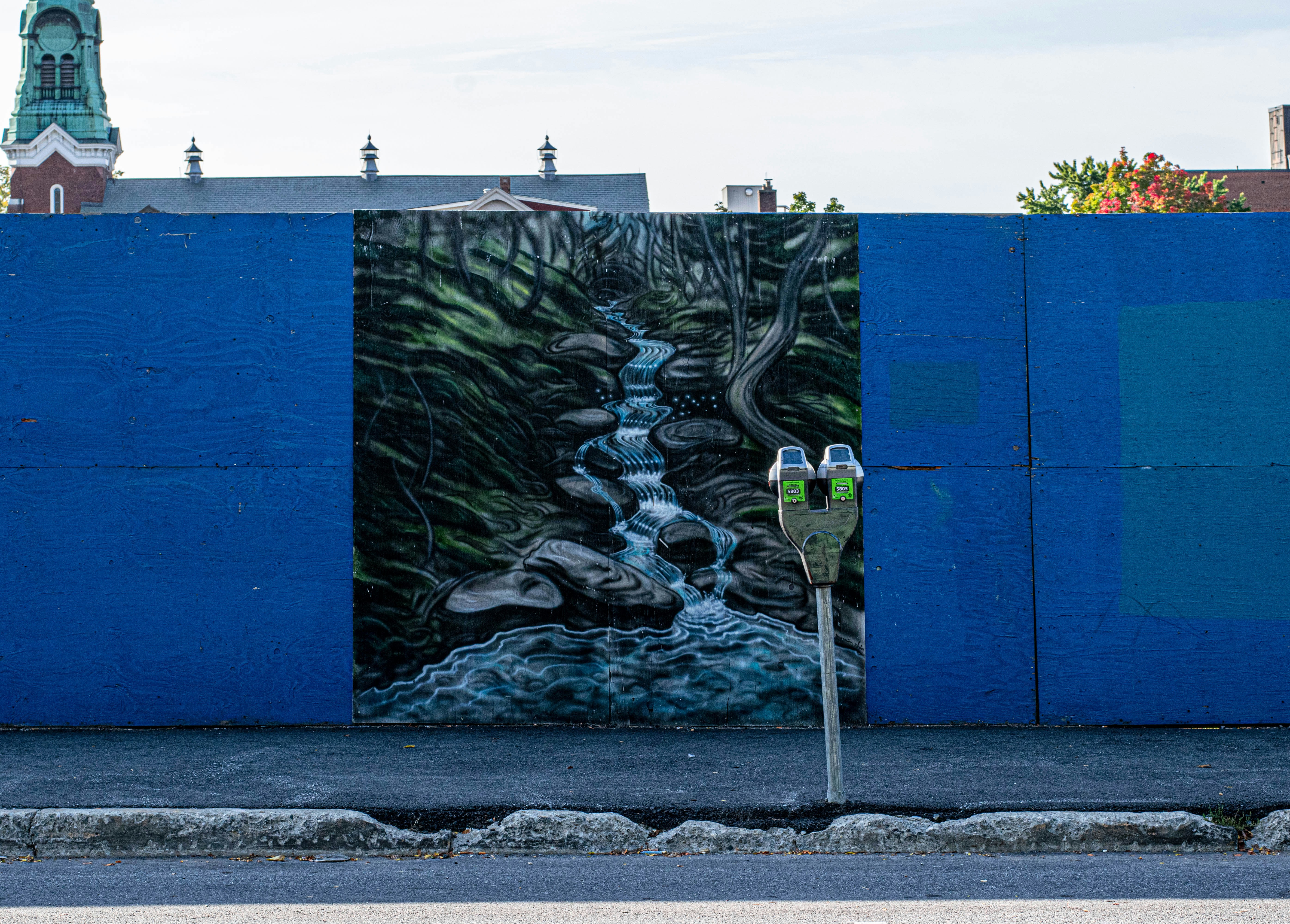 a parking meter sitting next to a blue wall with a painting on it