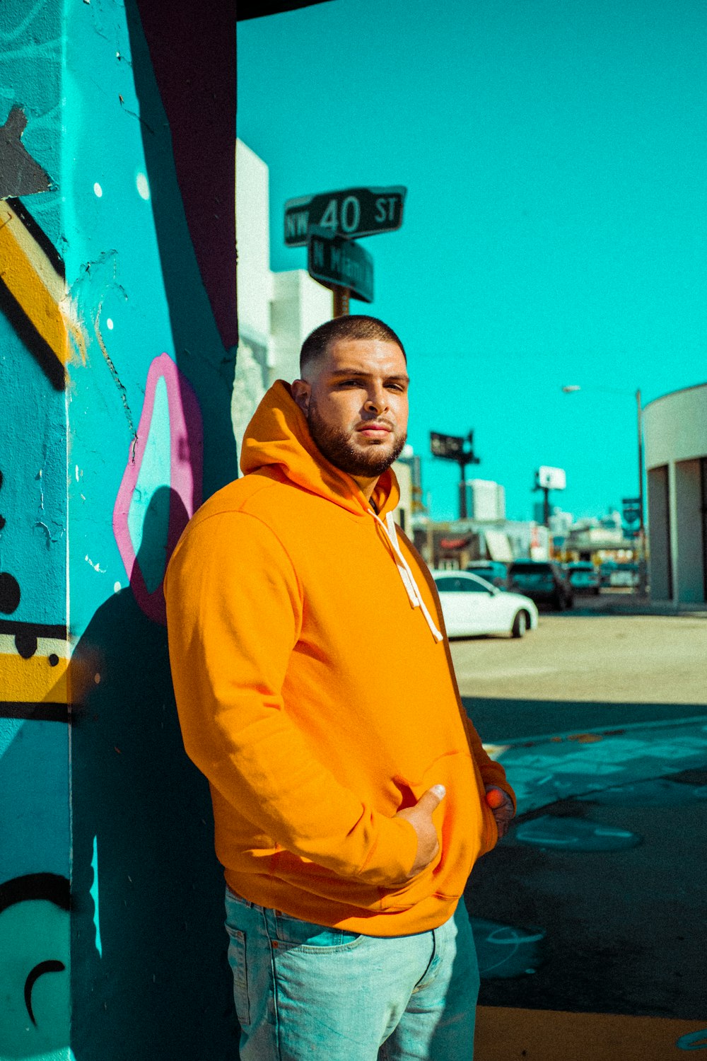 a man in an orange hoodie leaning against a wall