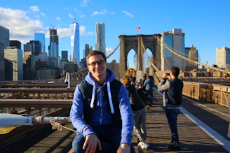 A smiling young person walking the streets of New York City with iconic skyscrapers in the background.