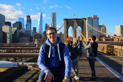 A smiling young person walking the streets of New York City with iconic skyscrapers in the background.