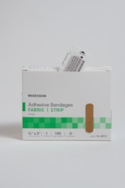 A box of adhesive bandages branded as McKesson, with a simple and clean packaging design. The box has a green checkered pattern and contains fabric strip bandages. A bandage packet is partially pulled out from the box.