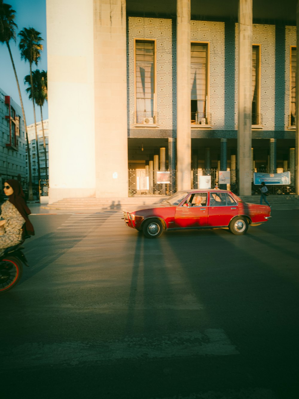 a red car driving down a street next to a tall building