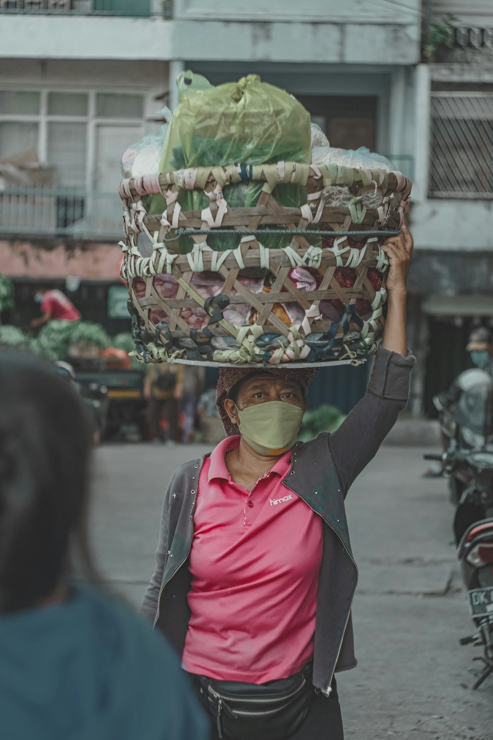 a woman wearing a face mask carrying a basket on her head