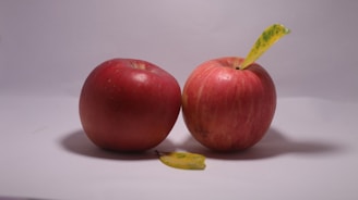 two red apples sitting next to each other on a white surface