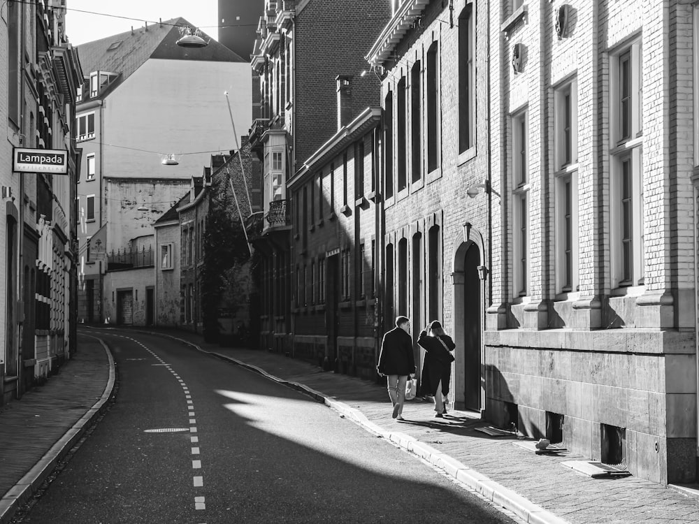 a couple of people walking down a street next to tall buildings