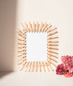 A decorative wooden frame with intricate patterns stands against a light background. To the side, a cluster of pink flowers adds a pop of color.