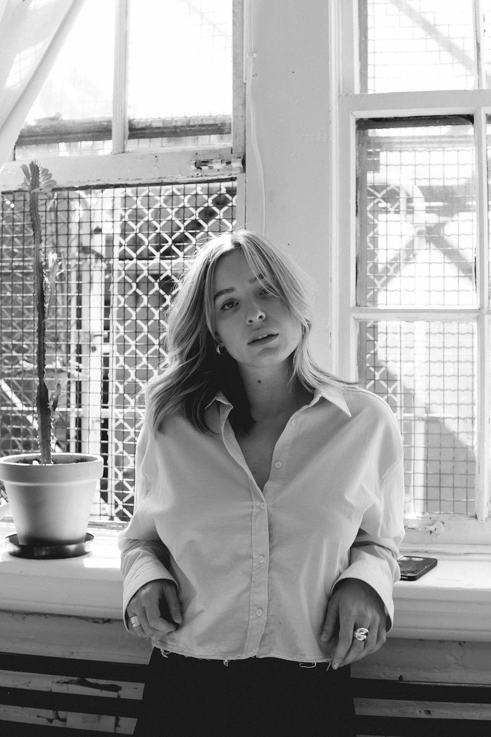 a black and white photo of a woman standing in front of a window