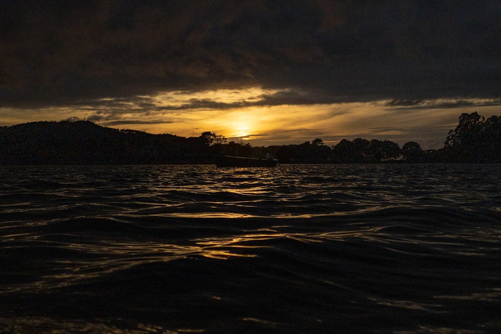 a boat floating on top of a body of water under a cloudy sky