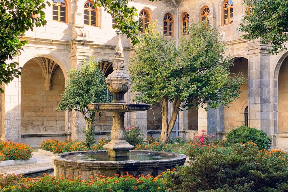 a fountain surrounded by flowers and trees in front of a building