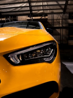 Side profile of a yellow compact car under bright showroom lights