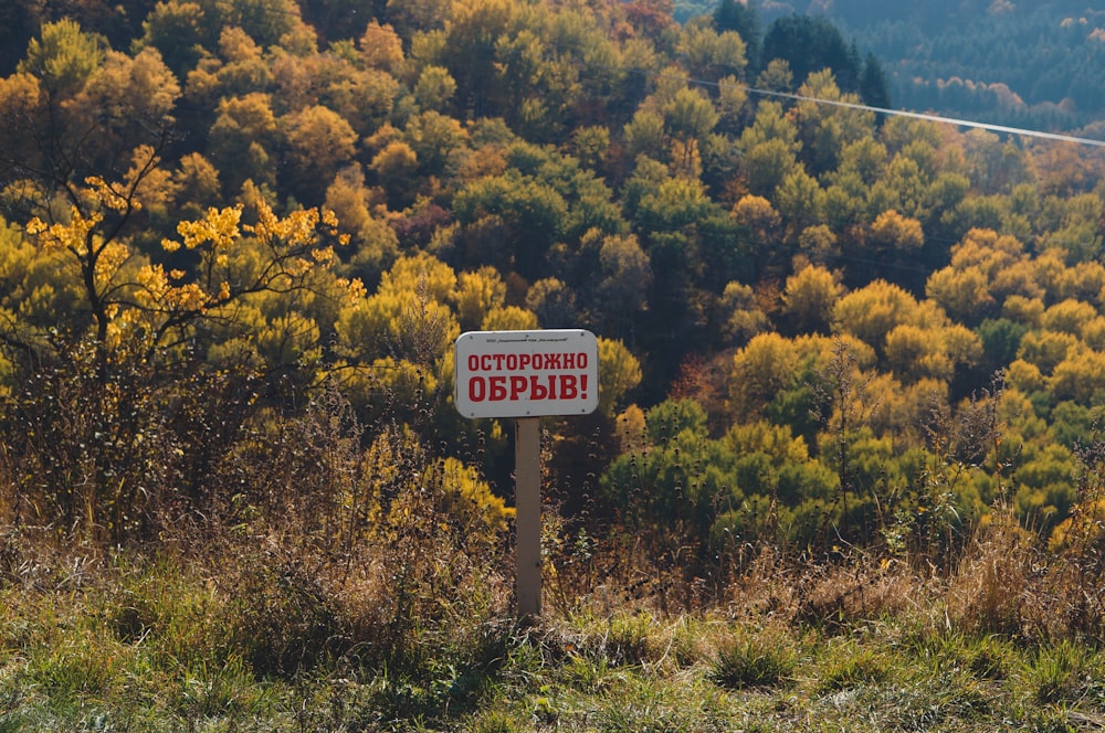 a red and white sign sitting on the side of a lush green hillside