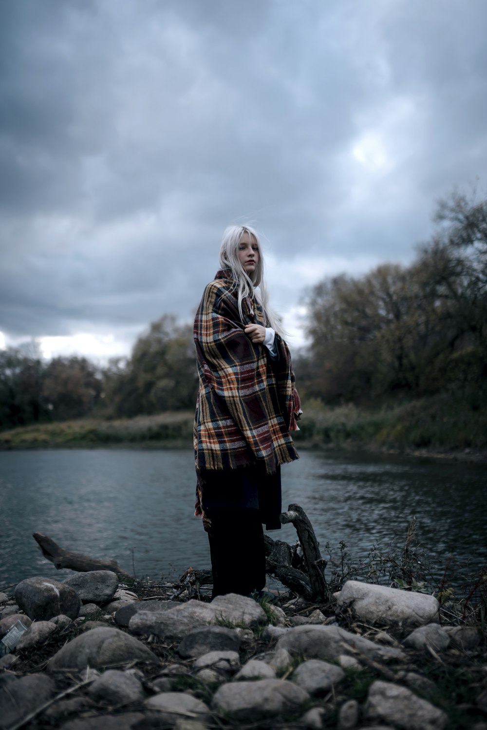 a woman standing on a rocky shore next to a body of water