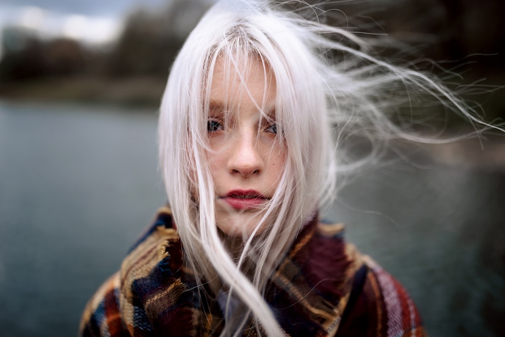 a woman with white hair standing by a body of water