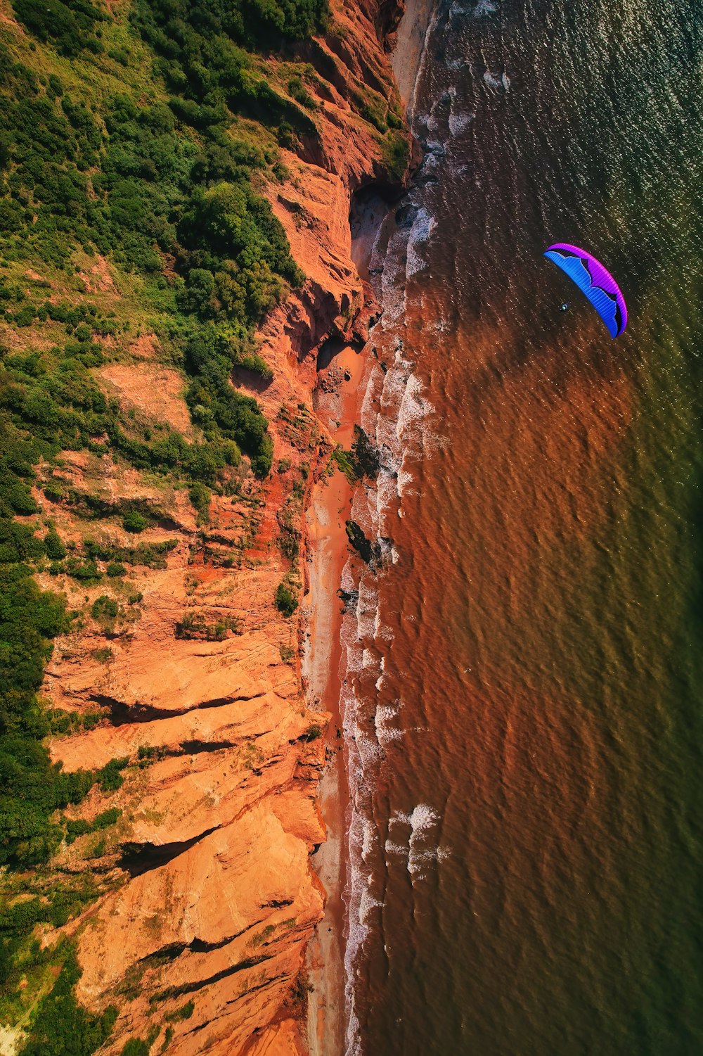 an aerial view of a beach with a parasail in the water