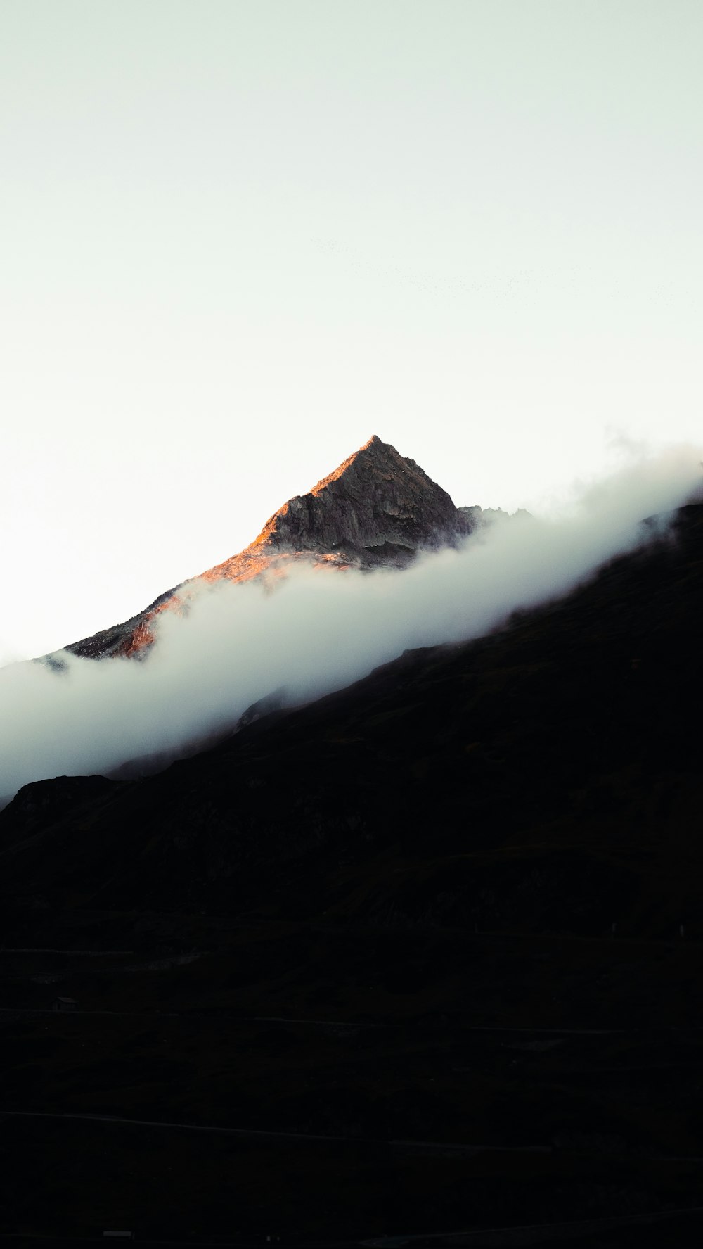 a mountain covered in clouds with a mountain in the background