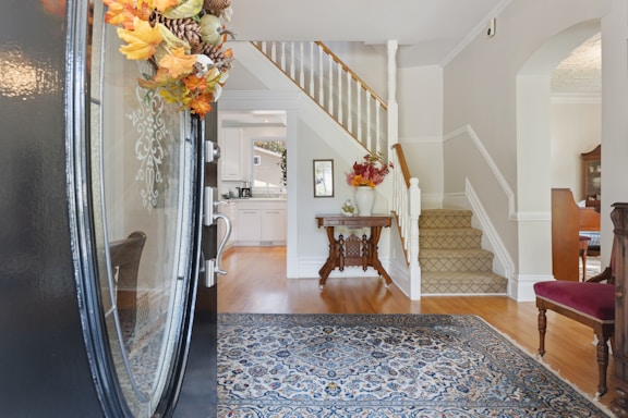 A cozy, sunlit home entryway with a vase of fresh flowers and a honeycomb-patterned doormat.