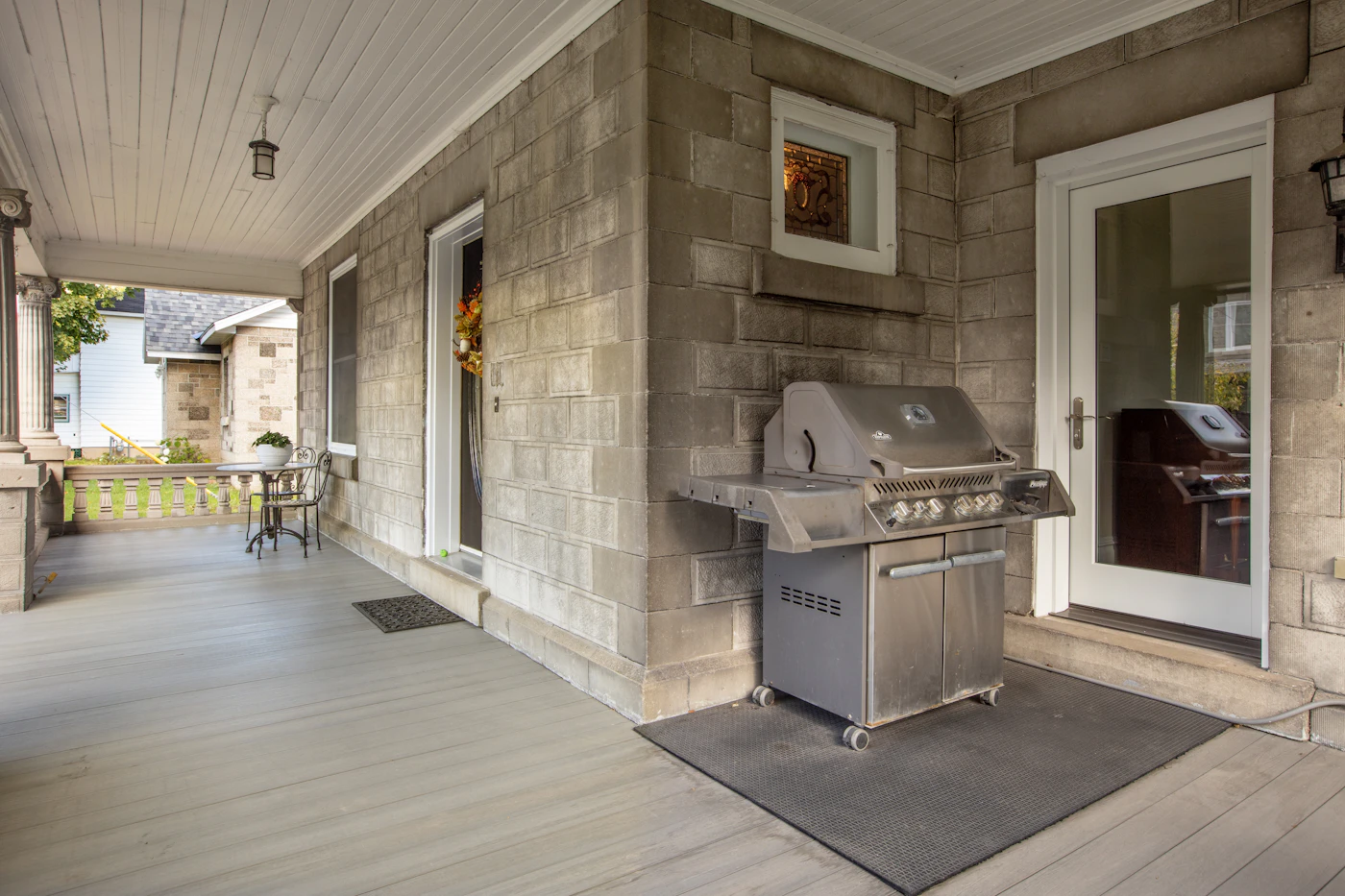 A covered front porch of a house with a grill set up on it.