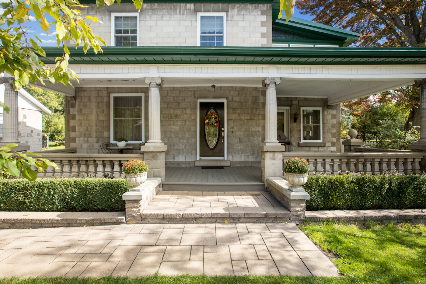 A stone house with a covered front porch and trimmed hedges