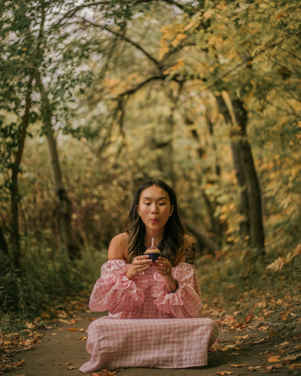 a woman in a pink dress sitting on a path in the woods