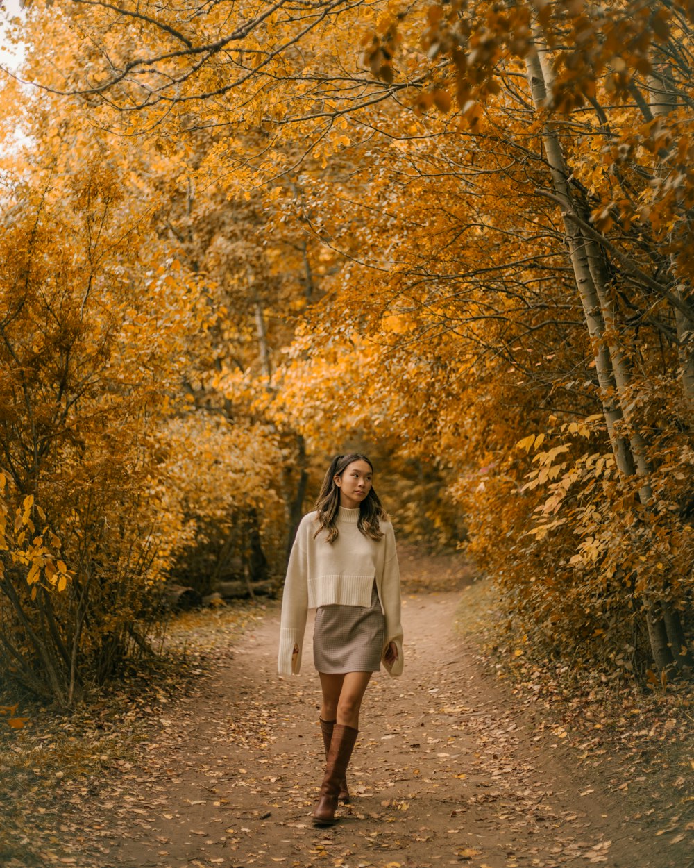 a woman walking down a dirt road surrounded by trees