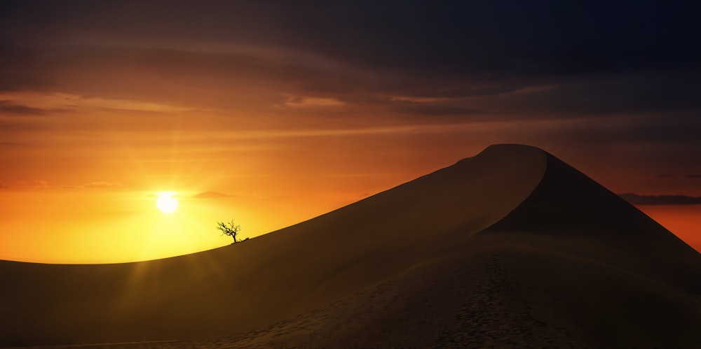 the sun is setting over a sand dune