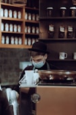 a man wearing a face mask behind a coffee machine
