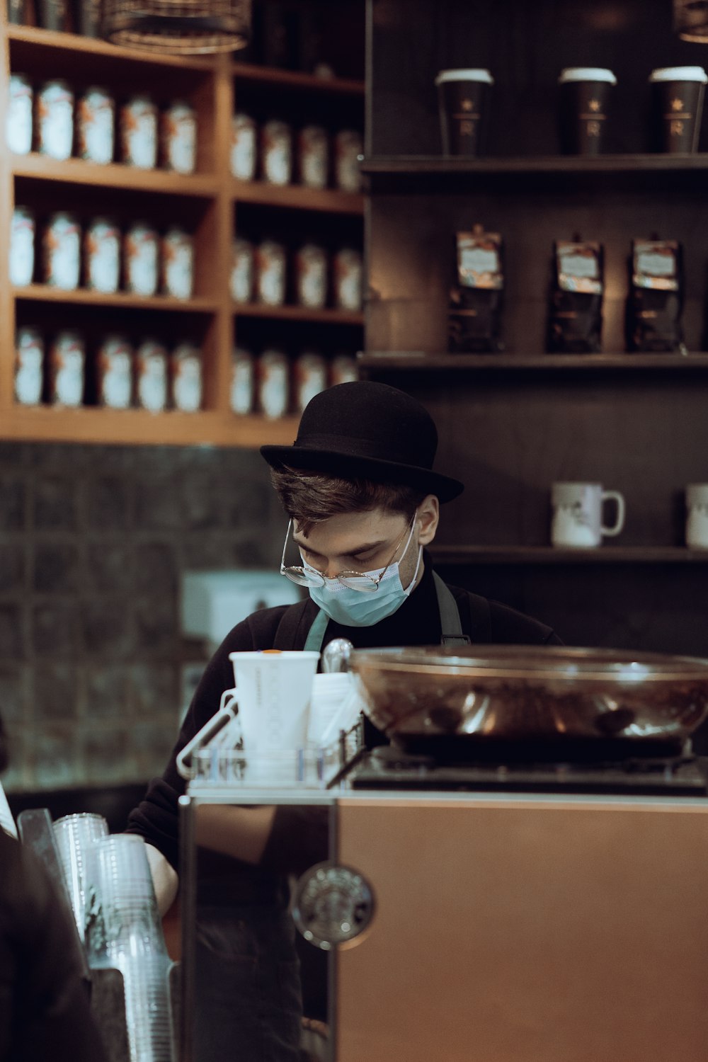 a man wearing a face mask behind a coffee machine