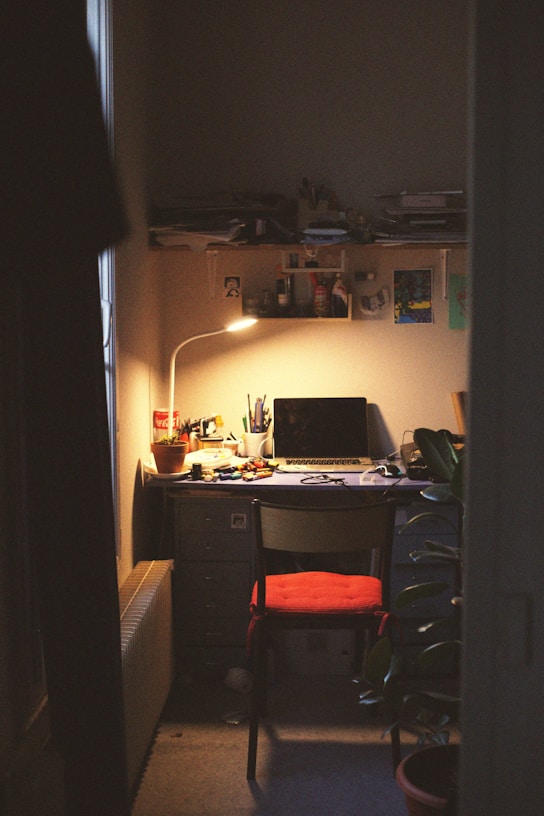 A cozy workspace bathed in soft pink light, with delicate paper goods and sketchbooks scattered gently around.