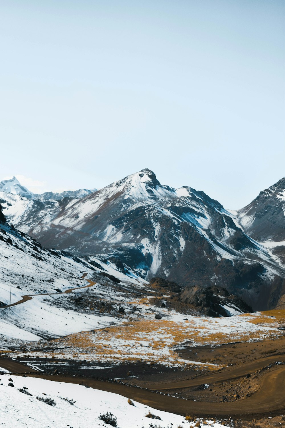 a mountain range covered in snow and brown grass