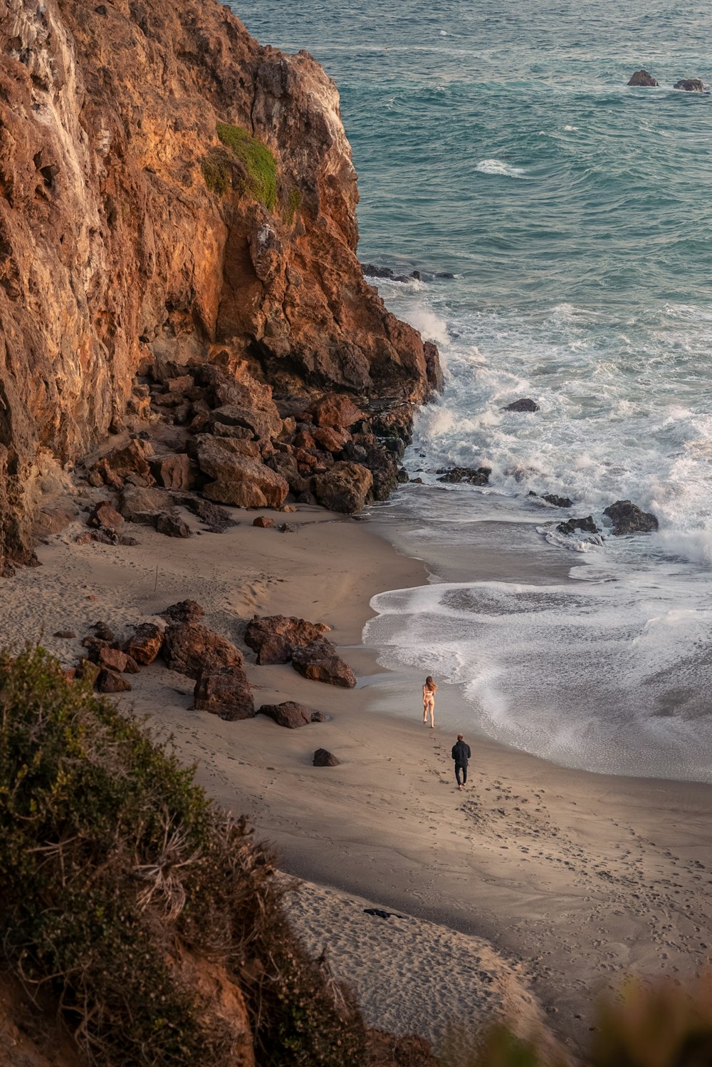 two people walking on a beach next to the ocean