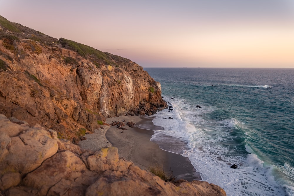 a rocky cliff overlooks the ocean with a boat in the distance